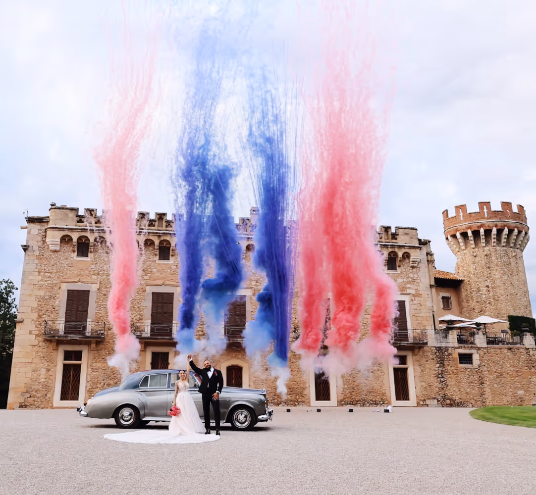 Ślub w Hiszpanii. Peralada. Para młoda stoi przed zamkiem, trzymając się za ręce. Za nimi wystrzelono konfetti.